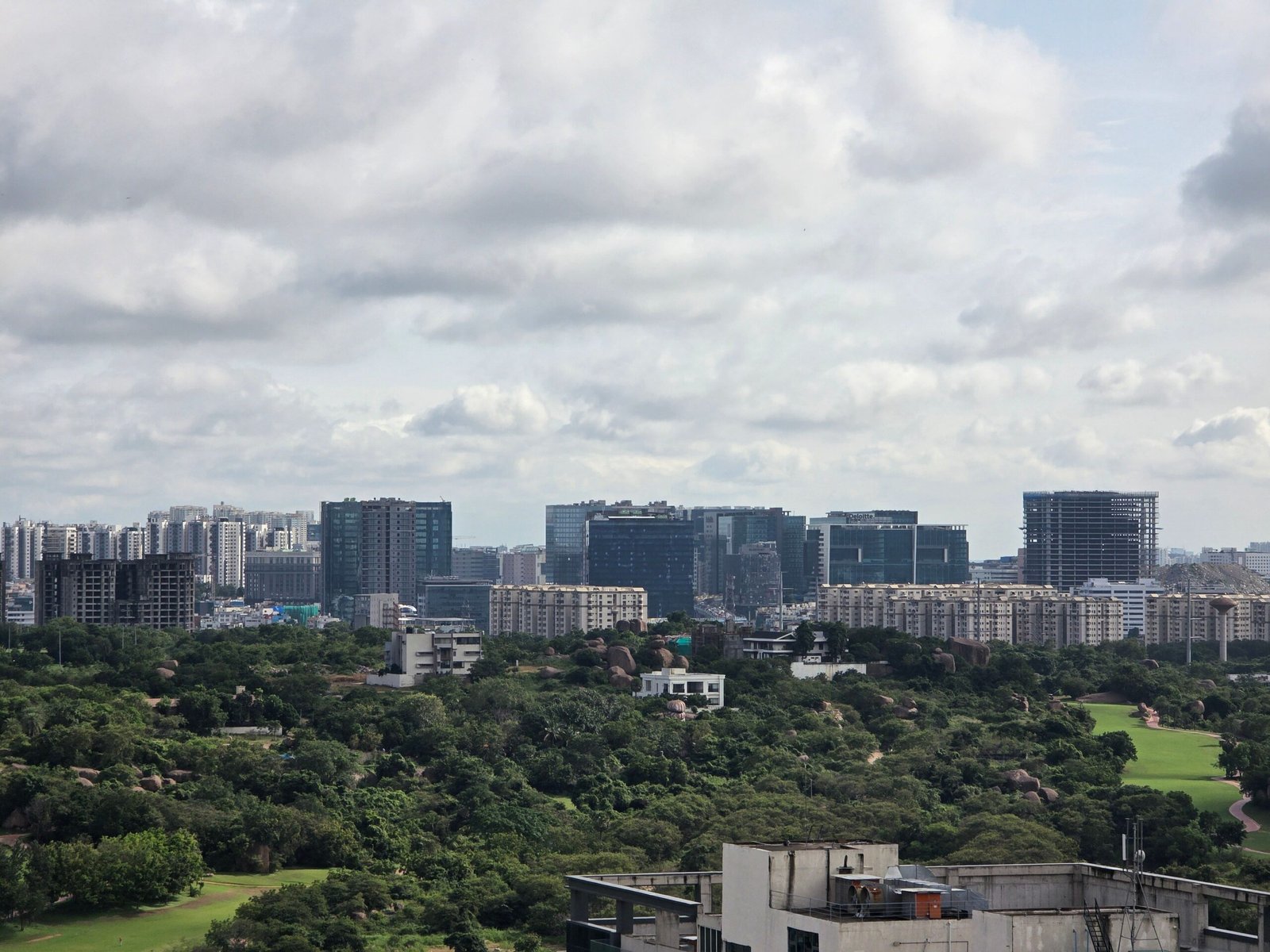 Modern skyline with lush green foreground and cloudy sky.